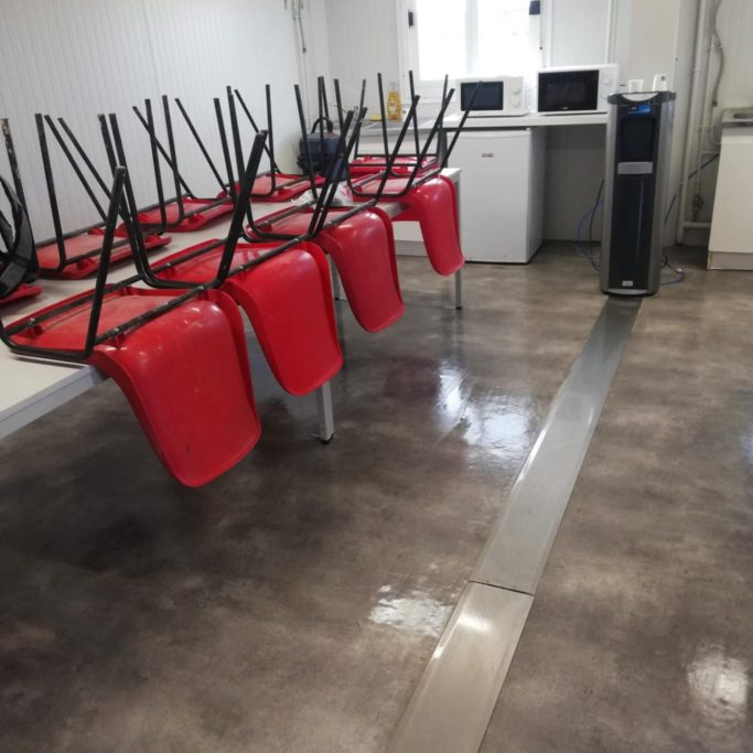 Salle vide avec des chaises rouges retournées et des électroménagers en arrière-plan.